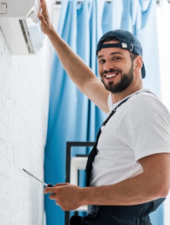 Smiling workman looking at camera while repairing air conditioner